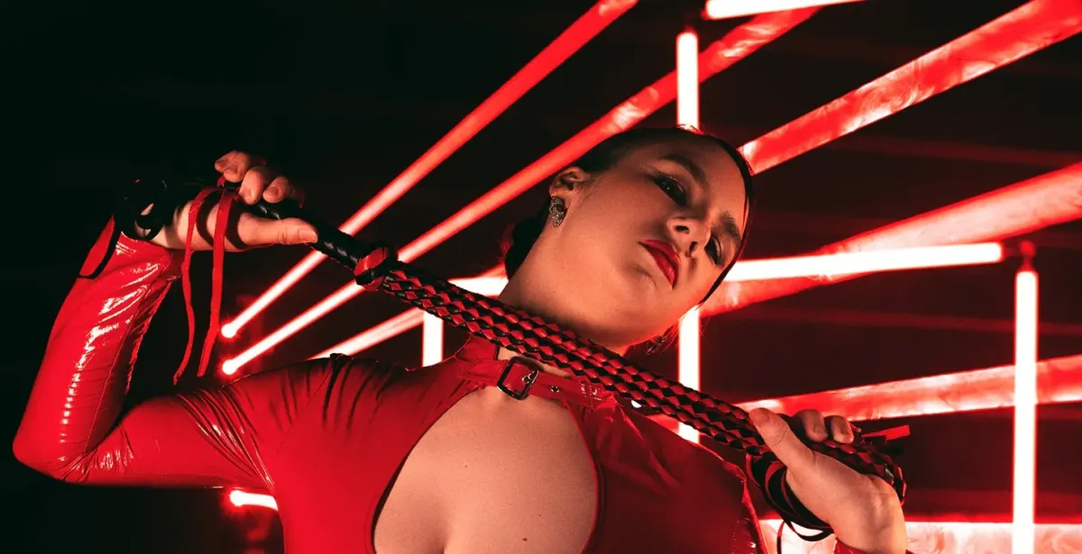 Person in red latex holding a braided cord, used as a BDSM-themed hero for kink-aware dating app alternatives