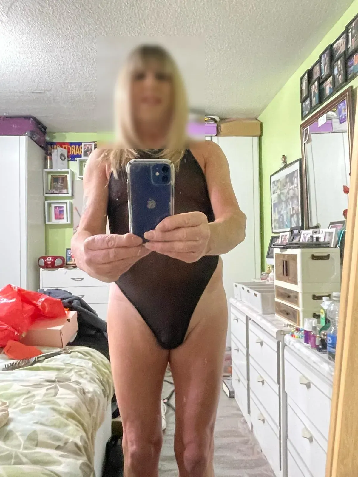 Person in a dark one-piece swimsuit taking a mirror selfie in a bedroom for kink dating app review context