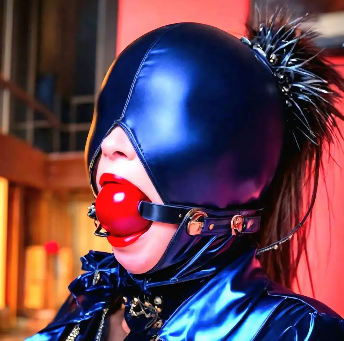 Side-profile close-up of a person in a shiny blue hood with a red gag ball, relevant to privacy considerations in kink dating.