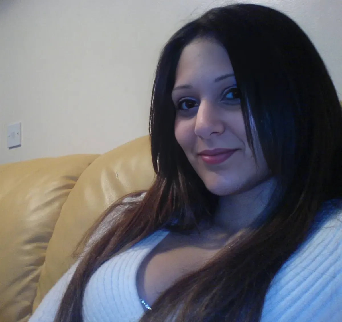 Adult woman in a white knit sweater seated on a tan couch for a privacy-focused dating comparison